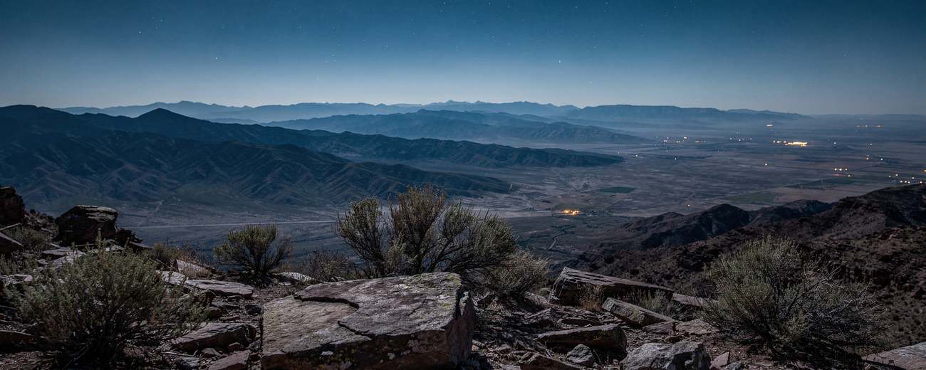 Basin-and-range country from height at the end of night, valley lights far below.