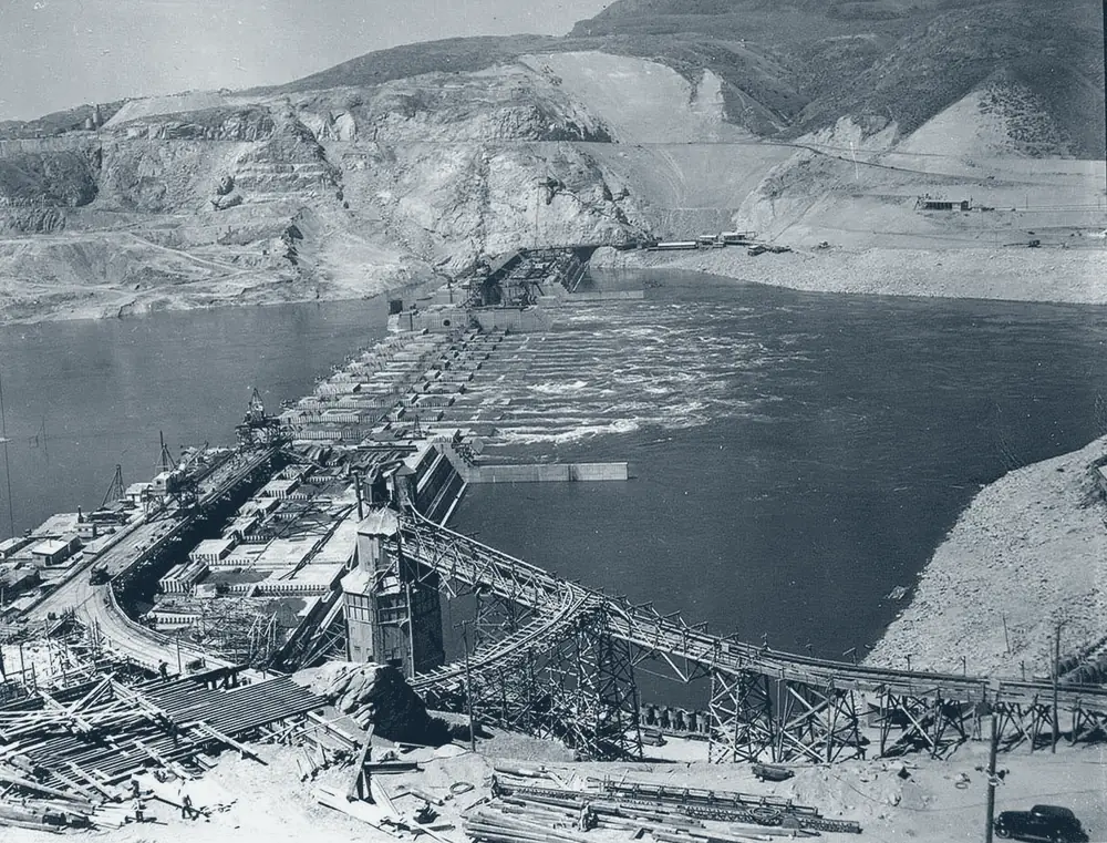 Grand Coulee Dam under construction in 1936: cofferdams, trestles and conveyor works spanning the Columbia between excavated abutments.