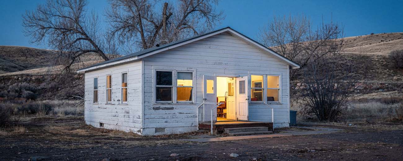 A clapboard community hall at dusk, doors open to warm light.